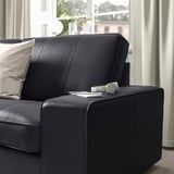 Schwarzes Ledersofa mit Armlehne, Kopfhörern und Fernbedienung an der Armlehne, an einem Fenster mit Vorhängen.