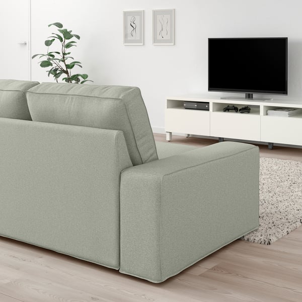 Modernes Wohnzimmer mit KIVIK-Sofa in Hellgrün, Flachbildfernseher, weißem Schrank und Wandkunst. Die Größe der Sofas ergänzt den Fernseher und den Schrank.
