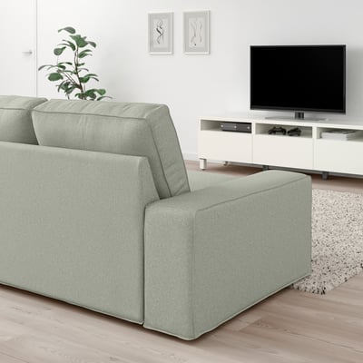 Modernes Wohnzimmer mit KIVIK-Sofa in Hellgrün, Flachbildfernseher, weißem Schrank und Wandkunst. Die Größe der Sofas ergänzt den Fernseher und den Schrank.