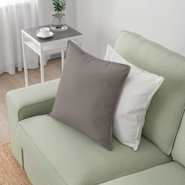 Gemütliches grünes Sofa mit grau/weißen Kissen in minimalistischem Zimmer. Beistelltisch mit Vase und Tassen.