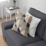 Graues Sofa mit abnehmbaren Kissen, eines davon gemustert, in der Nähe eines Beistelltisches mit Pflanze und Tasse.