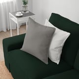 Dunkelgrünes Sofa mit grauen und weißen Kissen, daneben ein weißer Beistelltisch mit Vase und Tassen.