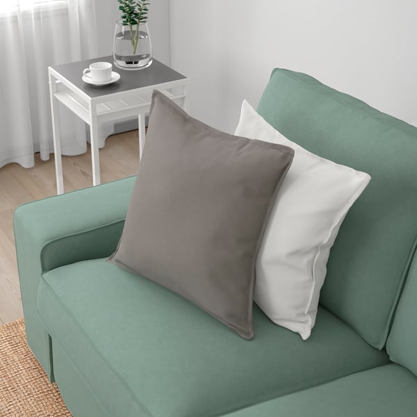Ein grünes KIVIK-Sofa mit grauen und weißen Kissen, das sein bequemes und einladendes Design zur Schau stellt und sich perfekt zum Entspannen eignet.