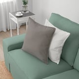 Ein grünes KIVIK-Sofa mit grauen und weißen Kissen, das sein bequemes und einladendes Design zur Schau stellt und sich perfekt zum Entspannen eignet.