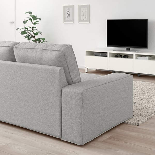 Modernes Wohnzimmer mit hellgrauem KIVIK-Sofa, Flachbildfernseher, weißem Schrank, Pflanze und gerahmter Kunst an der Wand.