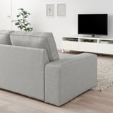 Modernes Wohnzimmer mit hellgrauem KIVIK-Sofa, Flachbildfernseher, weißem Schrank, Pflanze und gerahmter Kunst an der Wand.