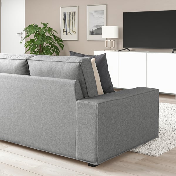 Modernes Wohnzimmer mit großem grauem KIVIK-Sofa, dunklen Kissen, Flachbildfernseher, weißem Schrank und Pflanze. Das Sofa ist geräumig und bietet Platz für mehrere Personen.