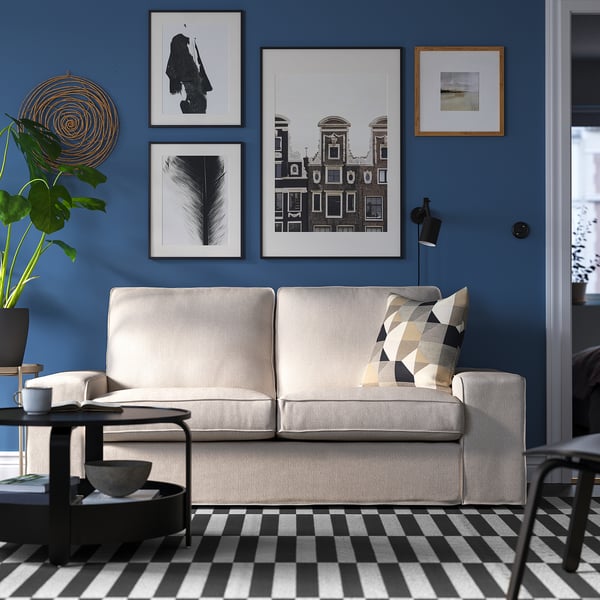 Modernes Wohnzimmer mit KIVIK-Sofa, kariertem Teppich, blauen Wänden und Wandkunst.