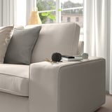 KIVIK Sofa mit grau/beigen Kissen in der Nähe eines Fensters, Bücher, Fernbedienung auf der Armlehne.
