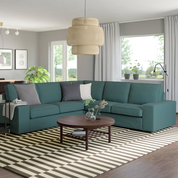 Teal KIVIK Sektionssofa mit modernem Design, groß und bequem, umgeben von gestreiftem Teppich, Couchtisch aus Holz und Hängelampe.