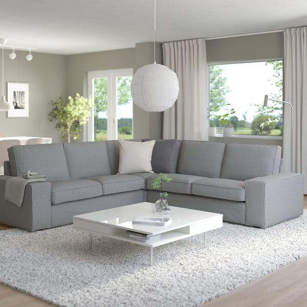 Modernes Wohnzimmer mit großem grauem KIVIK-Sofa, weißem Couchtisch und großem Fenster.