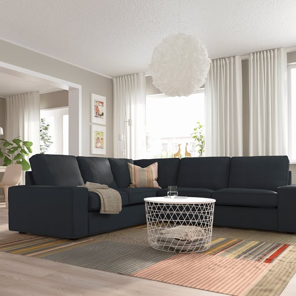 Großes, modernes Wohnzimmer mit einem dunkelgrauen KIVIK-Sofa, einem weißen Couchtisch, einem gestreiften Teppich, gemütlicher Beleuchtung und großen Fenstern mit Vorhängen.