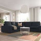 Großes, modernes Wohnzimmer mit einem dunkelgrauen KIVIK-Sofa, einem weißen Couchtisch, einem gestreiften Teppich, gemütlicher Beleuchtung und großen Fenstern mit Vorhängen.