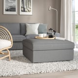 Grauer KIVIK Fußhocker im Wohnzimmer mit Stauraum, ergänzt blaues Sofa.