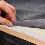 Eine Hand hält einen grauen zweifarbigen Sofabezug und zeigt den leicht zu reinigenden, maschinenwaschbaren Stoff.