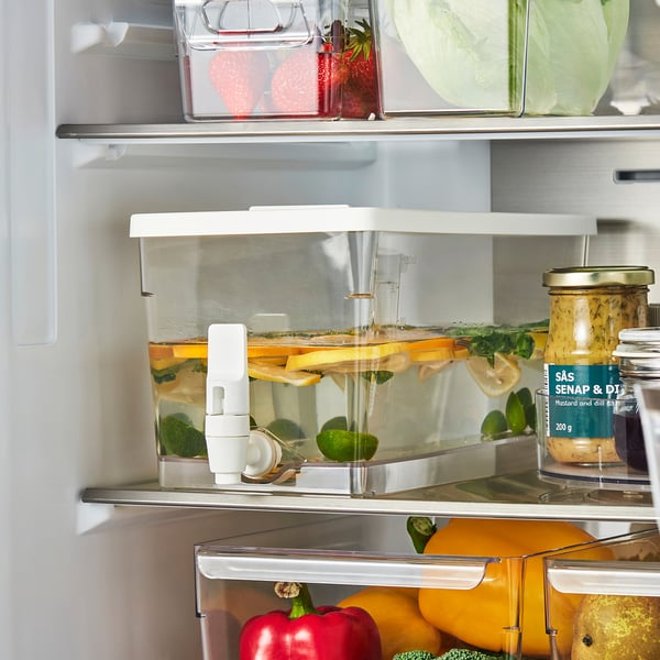 Offener Kühlschrank mit KLIPPKAKTUS-Behälter gefüllt mit Wasser, Fruchtscheiben und Eiswürfeln, bereit für die Ausgabe von gekühlten Getränken.