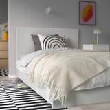 Gemütliches Schlafzimmer mit weißem Überwurf, Regenbogenkissen, großem Bett, gestreiftem Teppich. Weich, umweltfreundlich.