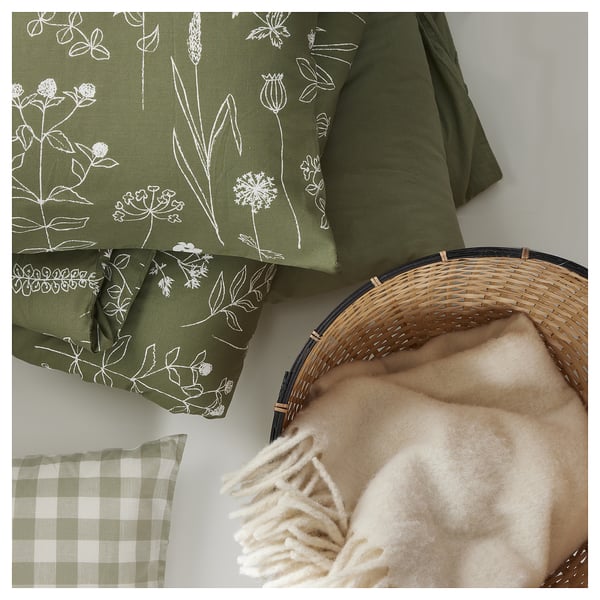 Olivgrün gemusterte Kissen, beige Decke mit Fransen, Weidenkorb, grün kariertes Kissen.