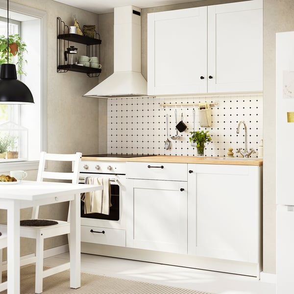 Moderne Küche mit Eichenarbeitsplatte, Hängetöpfen und Pflanzen. Weiße Schränke, Herd, Spüle und Essbereich.
