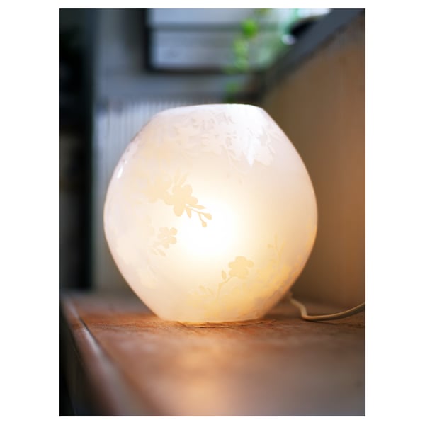 Eine kleine runde Lampe auf einer Holzoberfläche, die weiches, warmes Licht ausstrahlt. Es ätzte Kirschblüten-Designs und beleuchtete die komplizierten Muster.