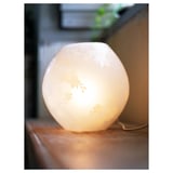 Eine kleine runde Lampe auf einer Holzoberfläche, die weiches, warmes Licht ausstrahlt. Es ätzte Kirschblüten-Designs und beleuchtete die komplizierten Muster.
