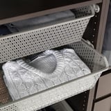 Metallgitterkorb, der den gefalteten Pullover im Schrank für die Luftzirkulation hält.