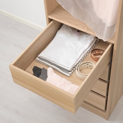 Offene Holzschublade mit gefalteter Kleidung und Accessoires, Teil des IKEAS KOMPLEMENT Aufbewahrungssystems.
