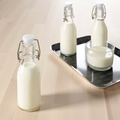 Drei Flaschen mit Flüssigkeit, zwei auf Tablett, eine separat, mit Glasbecher.