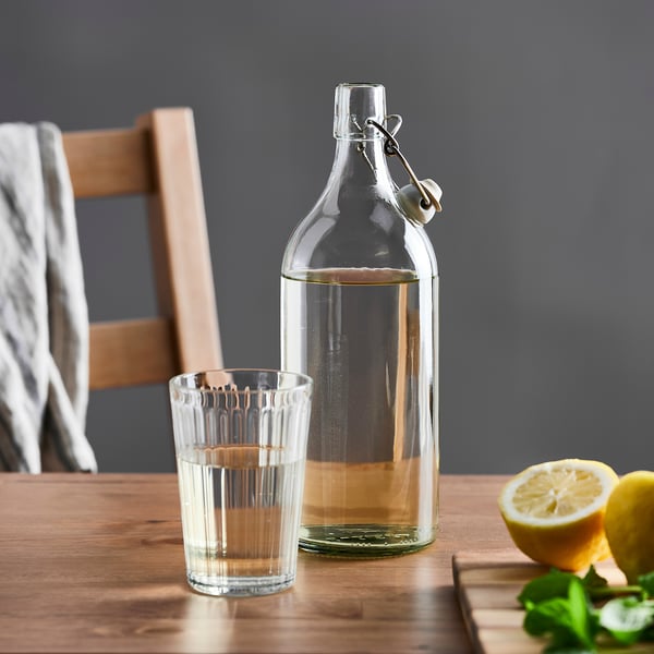 Klarglasflasche mit Stopfen auf Holztisch neben vollem Glas und Zitronen.
