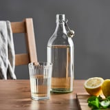 Klarglasflasche mit Stopfen auf Holztisch neben vollem Glas und Zitronen.