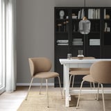 Modernes Essen mit KRYLBO-Stühlen um einen weißen Tisch. Schwarzes Bücherregal mit Dekor, Pendelleuchte aus Glas, hellgrauen Wänden und hellen Holzböden.
