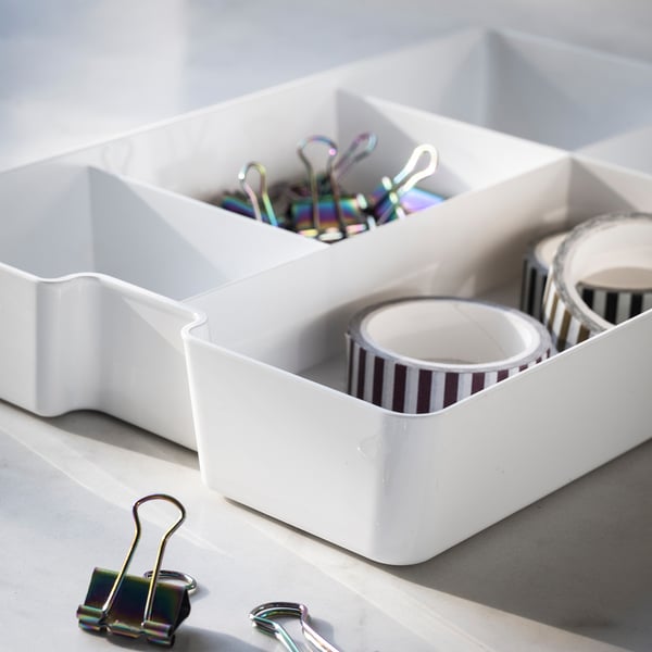 Weiße Organizer-Tabletts mit Schreibtischbedarf. Enthält bunte Clips und gestreiftes Klebeband.