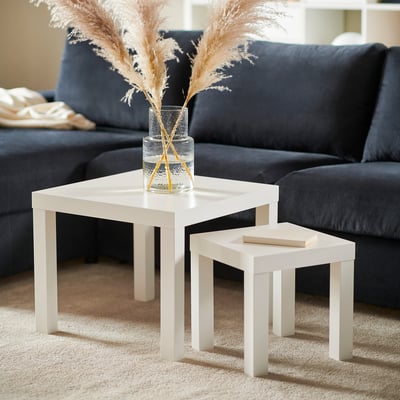 Wohnzimmer mit weißen LACK-Beistelltischen. Eine hält eine Vase mit getrockneten Blumen. Dunkelgraue Couch im Hintergrund.