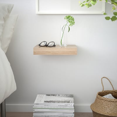 Minimalistischer Raum mit Regal für Gläser, Vasen und Zeitschriften. Geflochtener Korb und Bett ebenfalls zu sehen.
