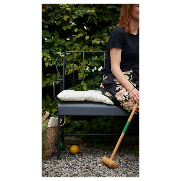 Person sitzt auf grauem LÄCKÖ Gartenstuhl mit Holzhammer, neben Korb auf Kies.