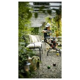 Frau im Garten Diamanten Terrasse, mit LÄCKÖ schwarzen Metallstühlen, Topfpflanzen, Tisch mit Zitrusfrüchten, Gläsern und Kerzen.