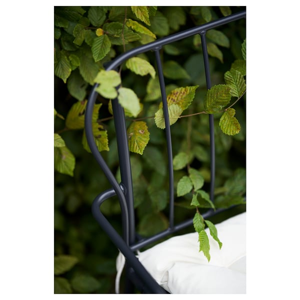 Dieses Bild zeigt einen Teil eines Gartenmöbelsets aus schwarz pulverbeschichtetem Stahl, wahrscheinlich LÄCKÖ, mit einem geschwungenen Design und grünen Blättern, die sich darum ranken.