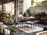 Gemütliche Terrasse LÄCKÖ schwarze Stühle mit grauen Kissen um einen Tisch, umgeben von Pflanzen und Lichterketten, die einen entspannenden Essbereich im Freien schaffen.