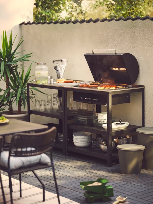 Schwarze Grillstation an Deck mit Speisen, Utensilien, Tellern und Tassen, die zum Essen eingerichtet sind.