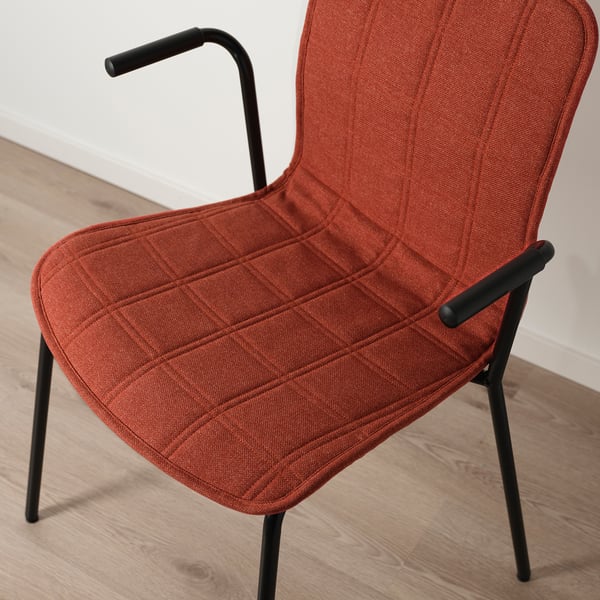 Leuchtend orangefarbener Polsterstuhl mit geschwungener Rückenlehne und Armlehnen auf schwarzen Metallbeinen.