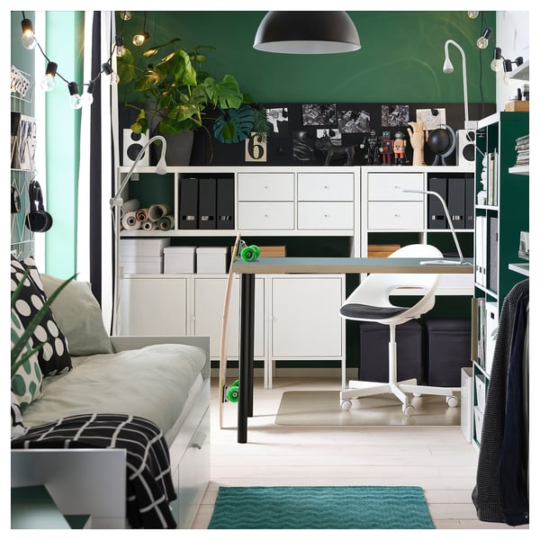 Modernes Homeoffice mit weißem Schreibtisch, Stuhl, grünem Teppich, Lichterketten und Pflanzen.