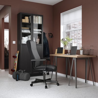 Einrichtung des Home-Office: schwarzer Schreibtisch, Stuhl, Bücherregal, braune Wände, Teppichboden.