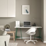 Ein minimalistisches Homeoffice mit einem weißen LAGKAPTEN-Schreibtisch mit grünen Beinen, einem weißen Bürostuhl, einem Laptop, einer Lampe und einem Kunstwerk.