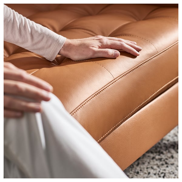 Hände testen eine mit braunem Leder gepolsterte Couch mit getufteter Rückenlehne.