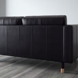Schwarzes Ledersofa mit gepolsterter Rückenlehne und Sitzfläche. Holzbeine mit goldenen Spitzen. Schlankes, modernes Design.