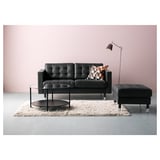 Modernes Wohnzimmer mit schwarzem Ledersofa, Couchtisch aus Glas, Stehlampe und zotteligem Teppich an rosa Wand.