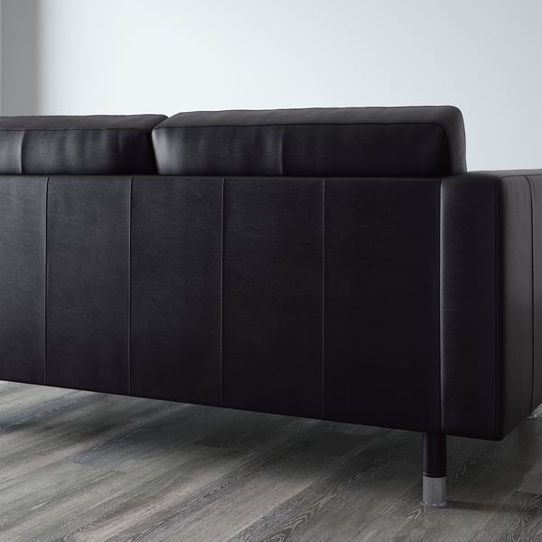 Schwarzes Ledersofa mit hochelastischen Schaumstoffkissen, das an einer minimalistischen Wand steht.