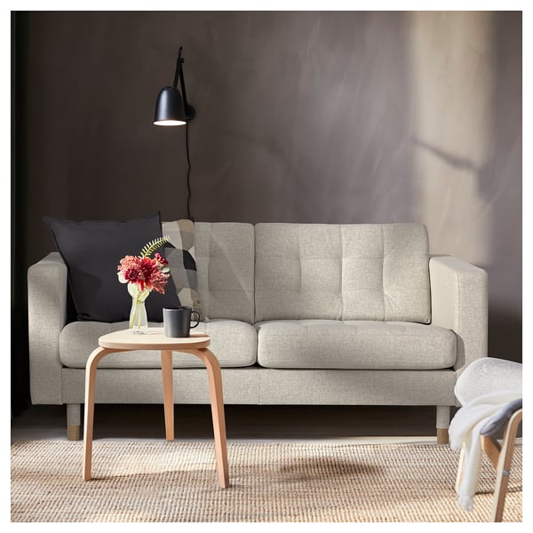 Modernes Wohnzimmer mit grauem LANDSKRONA-Sofa, schwarzem Kissen, Beistelltisch aus Holz, schwarzer Tasse, Blumenvase und Stehlampe.