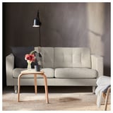 Modernes Wohnzimmer mit hellgrauem LANDSKRONA-Sofa, Beistelltisch aus Holz und schwarzer Wandleuchte. Dekorative Kissen und Vase mit Blumen auf dem Tisch.