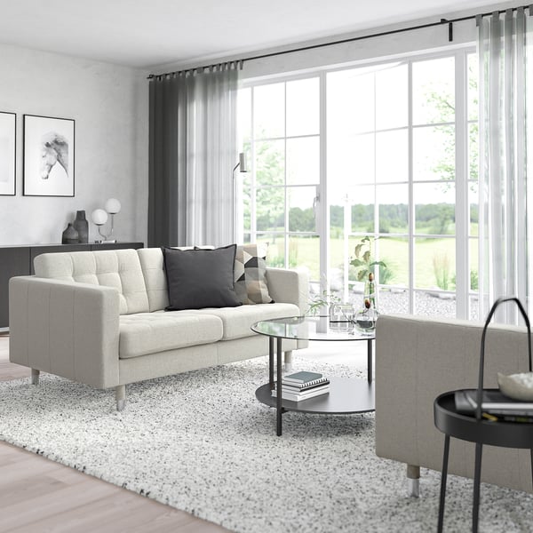 Modernes Wohnzimmer: weißes Sofa, Glastisch, gesprenkelter Teppich, Fenster mit Aussicht, minimalistische Einrichtung.